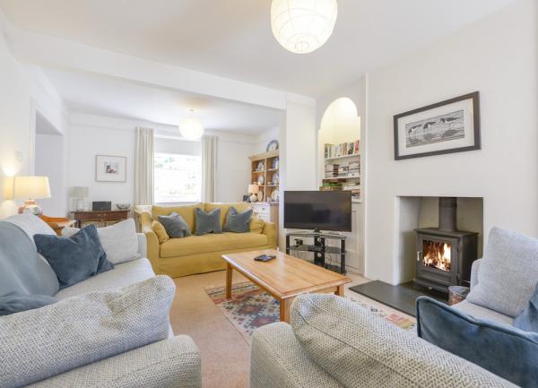 A lounge with sofas and armchairs group around a wooden coffee table facing a fireplace with a wood-burner.