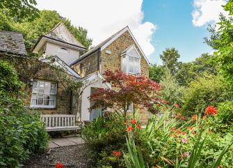A 2-storey Chideock holiday cottage with a tower surrounded by a flower-filled garden.
