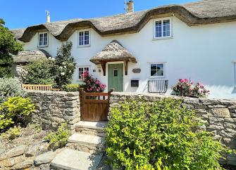 Exterior anf front garden of a double-fronted thatched holiday cottage in West Lulworth