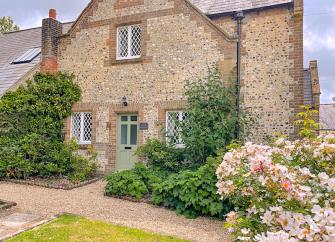 Gable end of a stone-built Dorset holiday cottage overlooking a shrub-filled front garden.