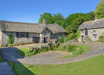 An ancient granite built and thatched Dartmoor longhouse overlooking a lawn.e