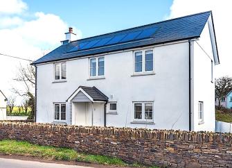 Exterior of a contemporary, slate-roofed holiday age surrounded by a low stone wall.