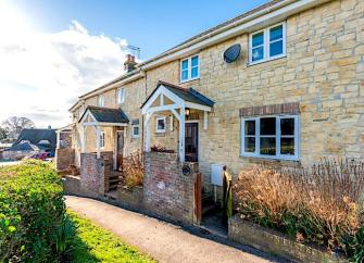 A limestone-built Dorset holiday cottage with a porch and tiny front garden.