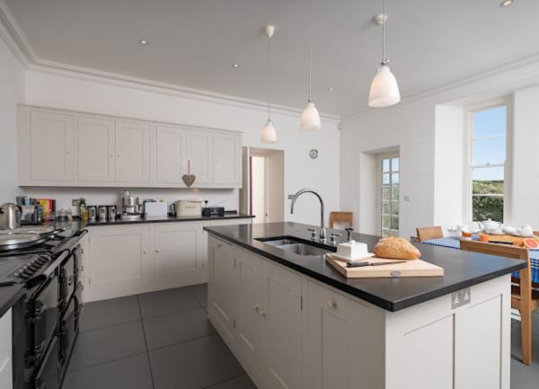 A spacious fitted kitchen with an Aga stove-dishwasher and an island containing the sink. A breakfast table offers lovely countryside views.