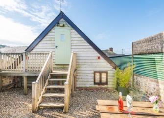 Gable end of a wood panelled Dorset barn conversion with wooden steps to a front door and deck.
