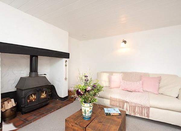 A Devon country cottage lounge with sofa and a wood burner in an inglenook fireplace.
