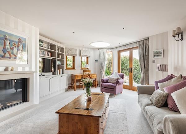 A luxurious lounge with sofas, armchair, TV, writing desk and wood-burner.