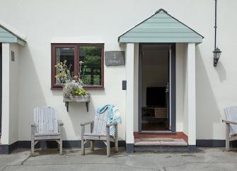 Wooden chair outside than open front door of a holiday cottage