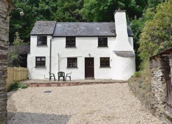 Exterior of an Exmoor country cottage with large chimney in front of tall trees and overlooking a large courtyard.