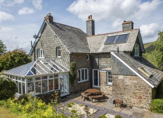 Exterior of a country house with sun room surrounded by beautiful gardens.