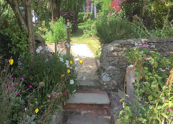 Steps through a gap in a stone wall lead to a flower-filled garden.