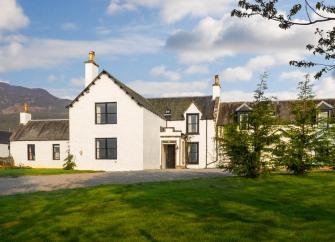 Exterior of a large country house with a Highland mountain in the background. 