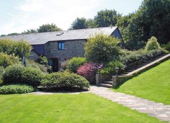 A stone-barn conversion surrounded by mature shrubs and trees.