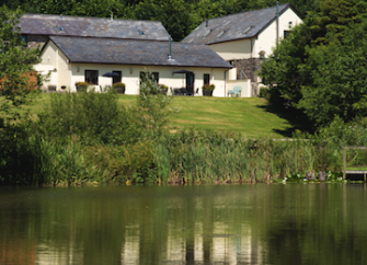 Barn conversions are reflected in the waters of a lake.