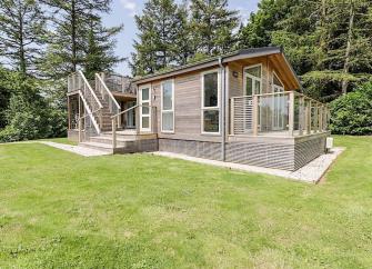 A wooden eco-lodge surrounded by a deck and a large lawn.
