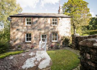 A stone-built, 2-storey cottage in Cumbria overlooks a large lawn.