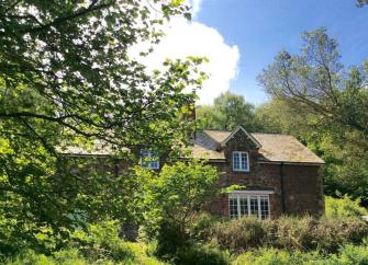 A two-storey holiday cottage seen through the branches of a tree.