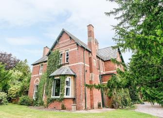 Brick-built Victorian vicarage surrounded by a tree-lined garden.