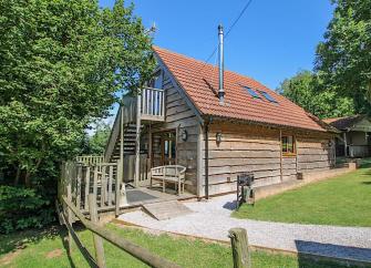 Large timber eco-holiday lodge with a hot tub and tree-lined lawn.