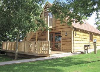 Exterior of a wooden eco-lodge with stairs to the 1st floor and a wide deck.