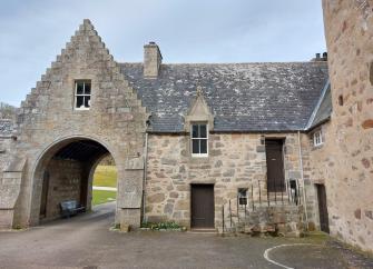 Entry arch and adjoining granite-built cottage overlook a castle courtyard.