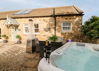 Exterior of a barn conversion overlooking a terrace with a hot tub.