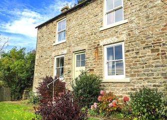 2-storey stone-built cottage overlooking a shrub-lined lawn.