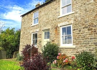 2-storey stone-built cottage overlooking a shrub-lined lawn.