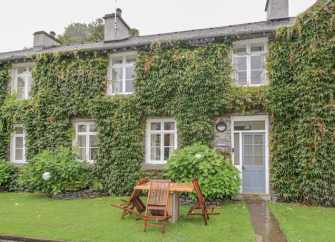 Ivy-clad exterior of a stone holiday cottage in Hawkshead, Cumbria, with a lawn to the front.