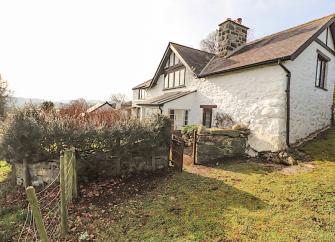 Exterior of a large whitewashed Welsh farmhouse and garden.