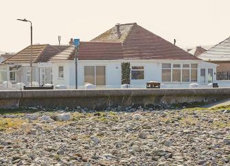 Exteerio of a beachfront chalet bungalow overlooking a sea wall.