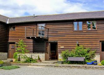 A woo-clad eco-cottage with a balcony overlooks a shrub-lined courtyard