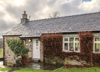 A stone-built,single storey holiday cottage with vine covered walls and a front garden.