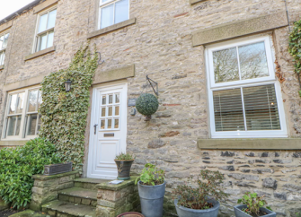 Stone built exterior of a Yorkshire Dales cottage with large zinc plant pots lining the front.