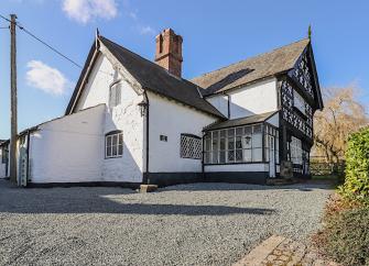 ATudor farmhouse with timbered beam and overhanging floor overlooks a mature garden.