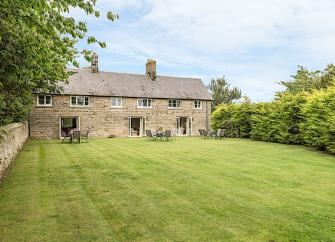 A long, stone-built cottage with 3 floor-to-ceiling ground-floor windows overlooking a spacious lawn. 