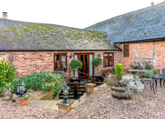 A single storey barn conversion overlooks a courtyard full of shrubs in large pots.