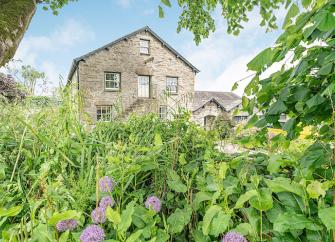 The 3-storey gable end seen through trees of a Cumbrian stone-barn conversion.