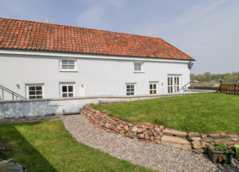 A rural holiday cottage with a terracotta roof sits behind a lawn with a shingled footpath.