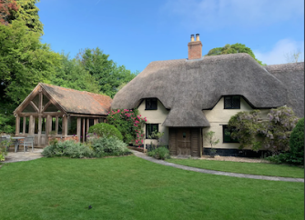 A thatched cottage with thatched porch and large conservatory overlooks a wide lawn.