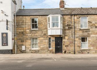 A stone-built terraced cottage with a large, 1st floor bay window overlooks a quiet street.
