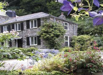 2-storey, granite-built cottage with many windows overlooks a mature garden.