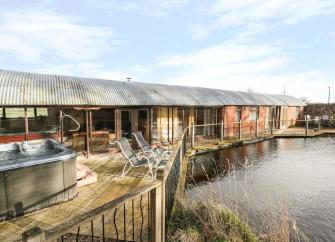 A row of wooden holiday lodges with a hot tub overlook a lake.