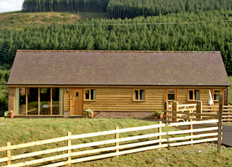 Exterior of a wooden eco-lodge with woods to the rear and open fields in the foreground.