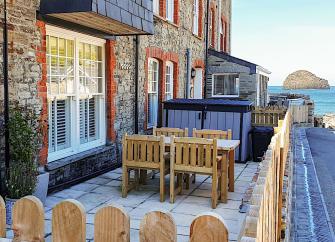 Stone built exterior of a Victorian, terraced holiday cottage with a fenced-in paved courtyard garden and sea views.