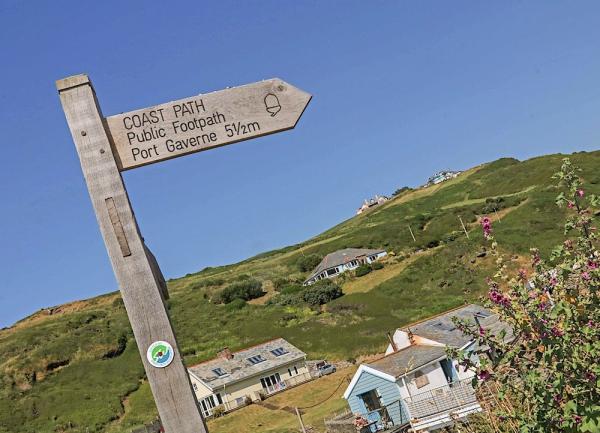 A coast path signpost overlooking a valley side with a handful of houses and bungalows scattered along it.
