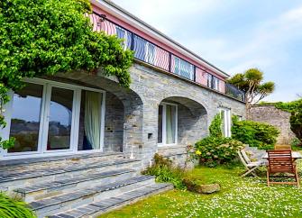 A wisteria-clad Tenby holiday cottage with floor-to-ceiling windows overlooks a daisy-filled lawn.