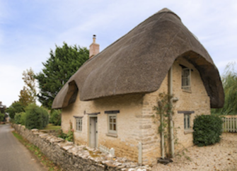 Exterior of a thatched 2-storey village holiday cottage in the Cotswolds.