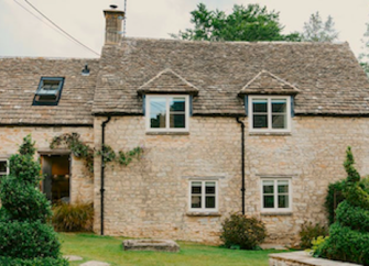 Exterior of a honey-coloured Cotswold holiday cottage with a spacious lawn with topiary.