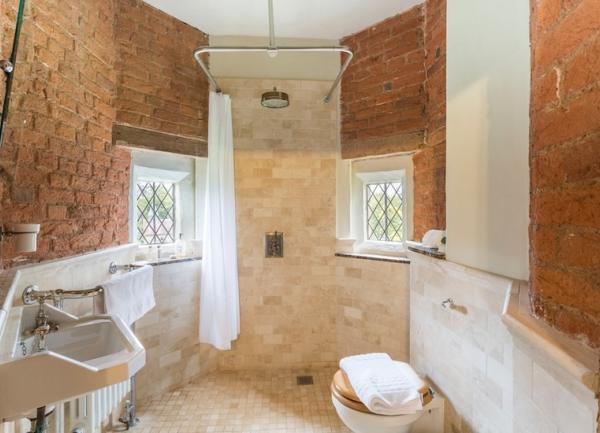 A wetroom with walk-in shower, WC, washbasin and exposed brick walls.